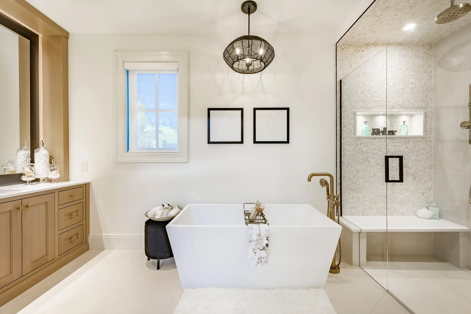 Large primary bathroom en suite. The bathroom has a freestanding bathtub and a very large shower with glass enclosure. A very large mirror and white countertop. The cabinets are a light wood and there is a bathrobe hanging on the shower door.